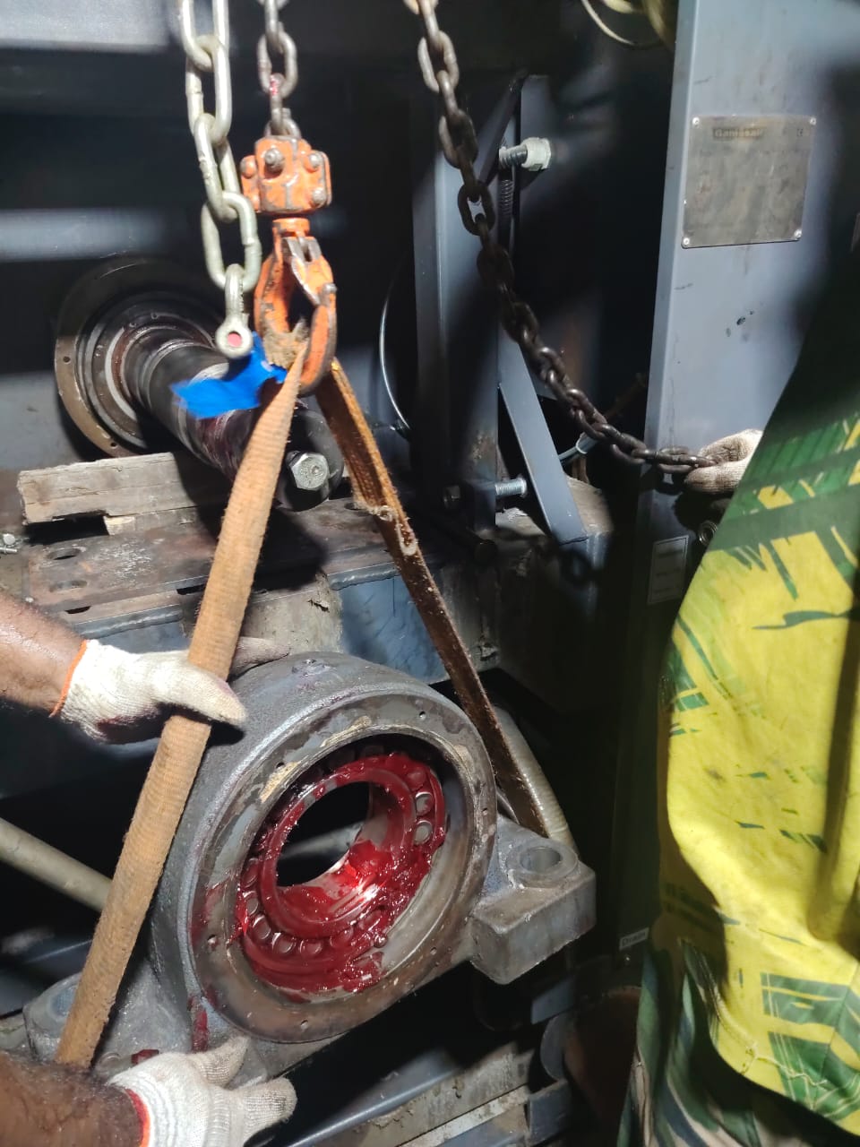 Opened bearing housing packed with red grease while a shaft hangs from a sling