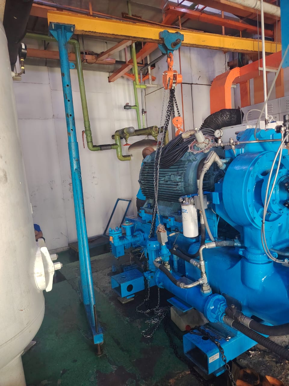 Blue screw air compressor with its motor suspended from a chain hoist