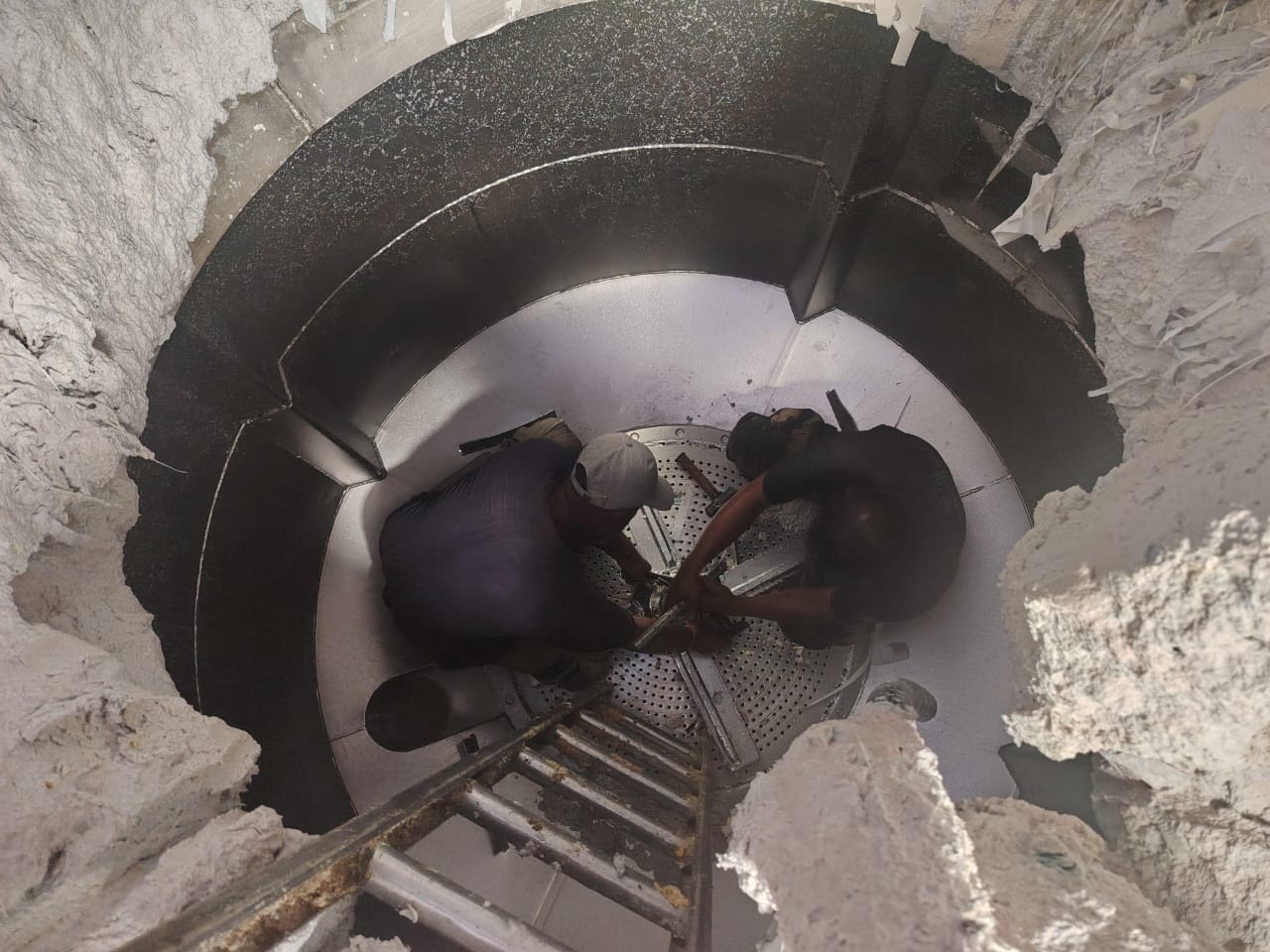 View looking down into a large vessel where two technicians work on the floor plate